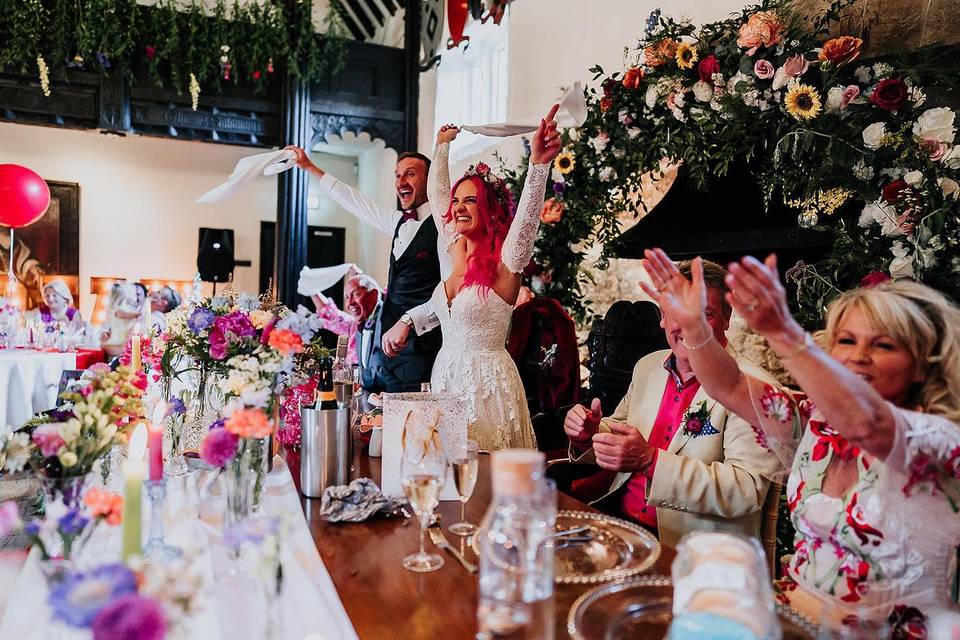 a couple and their top table guests all cheer and wave napkins at a colourful reception