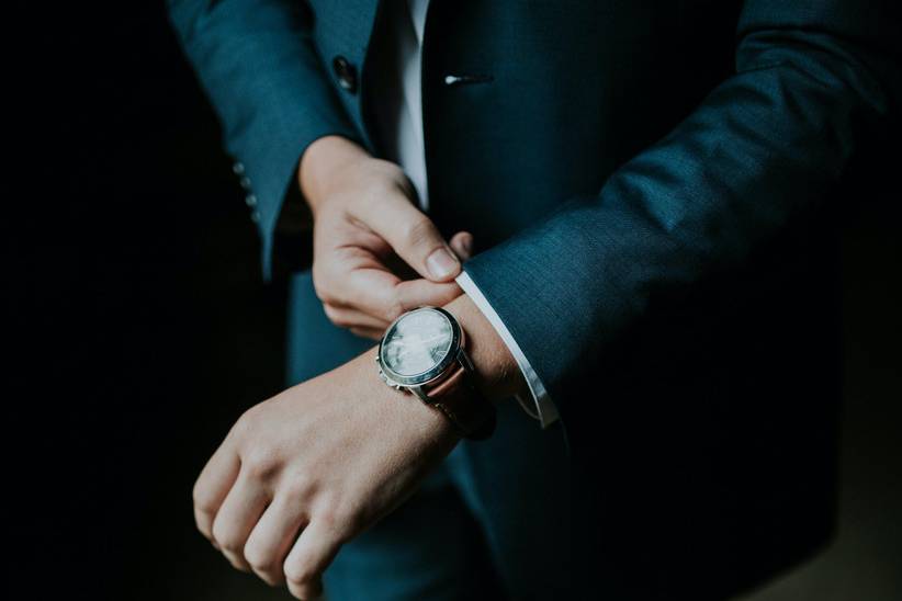 Groom wearing a suit adjusting his cuffs with a wedding watch visible on his wrist