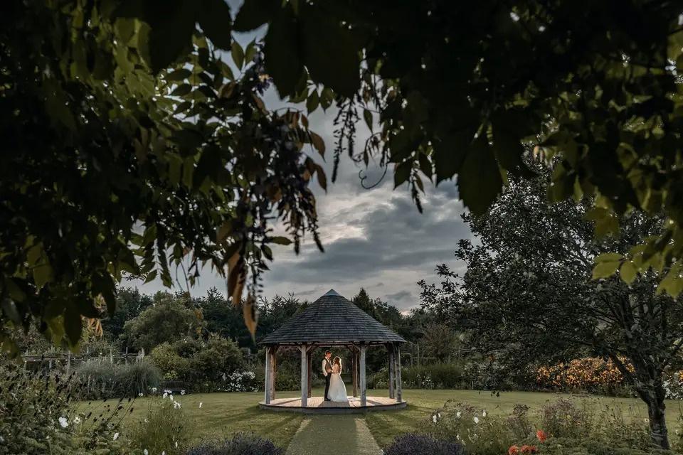 Bride and groom standing under a gazebo in an alice in wonderland themed wedding venue