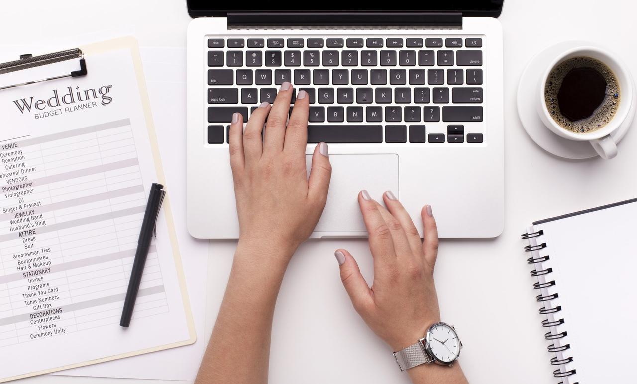 Person typing on a laptop next to a notebook and a cup of coffee