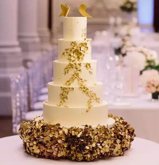 gold and white wedding cake with cascading gold leaves and a pair of golden birds as a cake topper