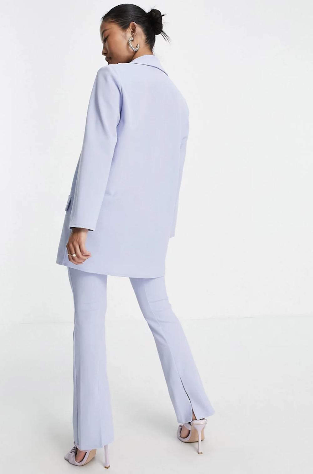 Asian woman with black hair slicked into a bun photographed from behind wearing chunky pearl hoop earrings and a lavender blue trouser suit with strappy heels