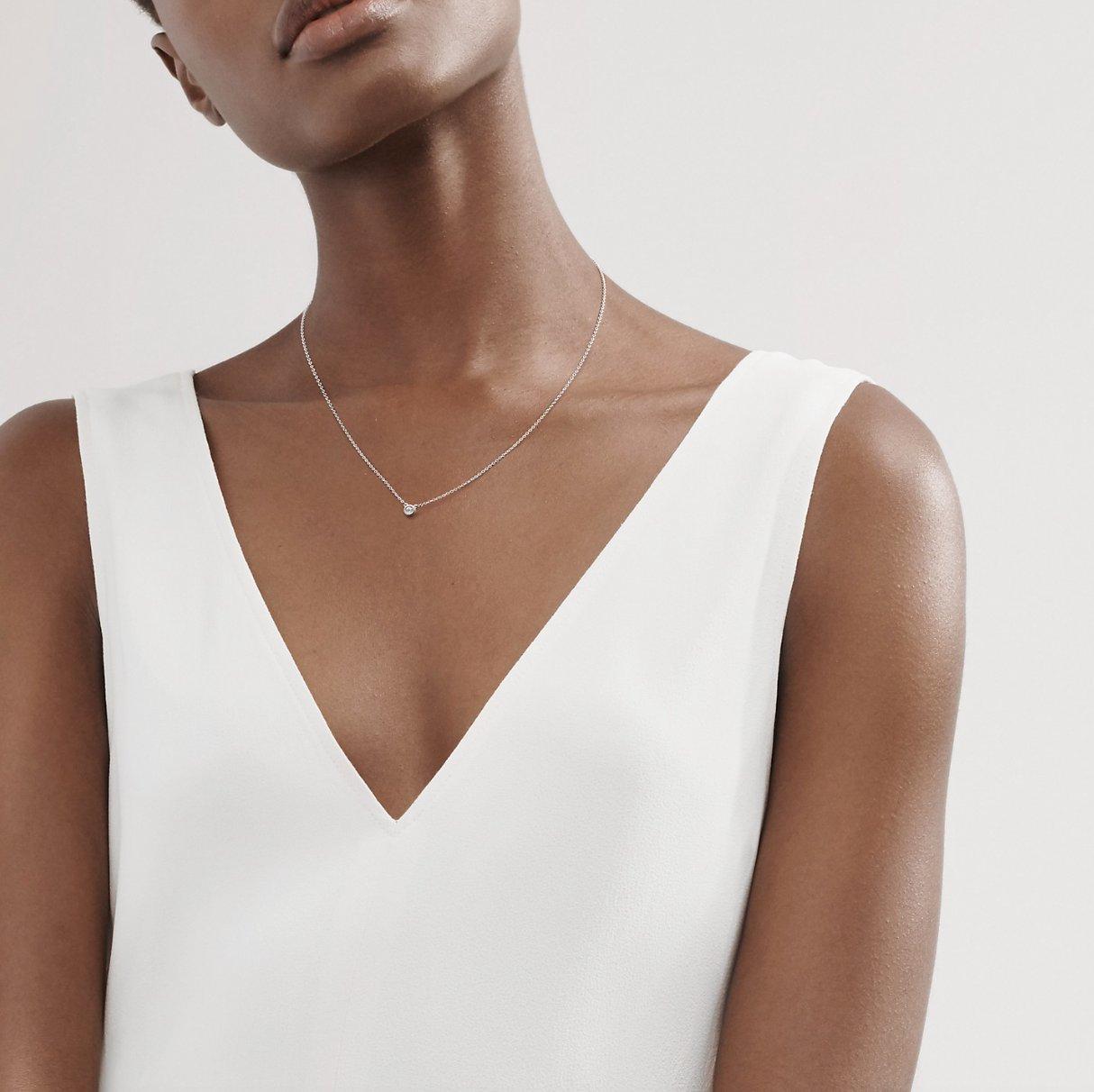 Black woman with short hair wearing a v-necked white top and delicate silver and aquamarine pendant necklace