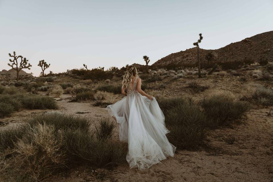 White woman with long blonde hair in braids running through the desert in a flowing sleeveless white wedding dress