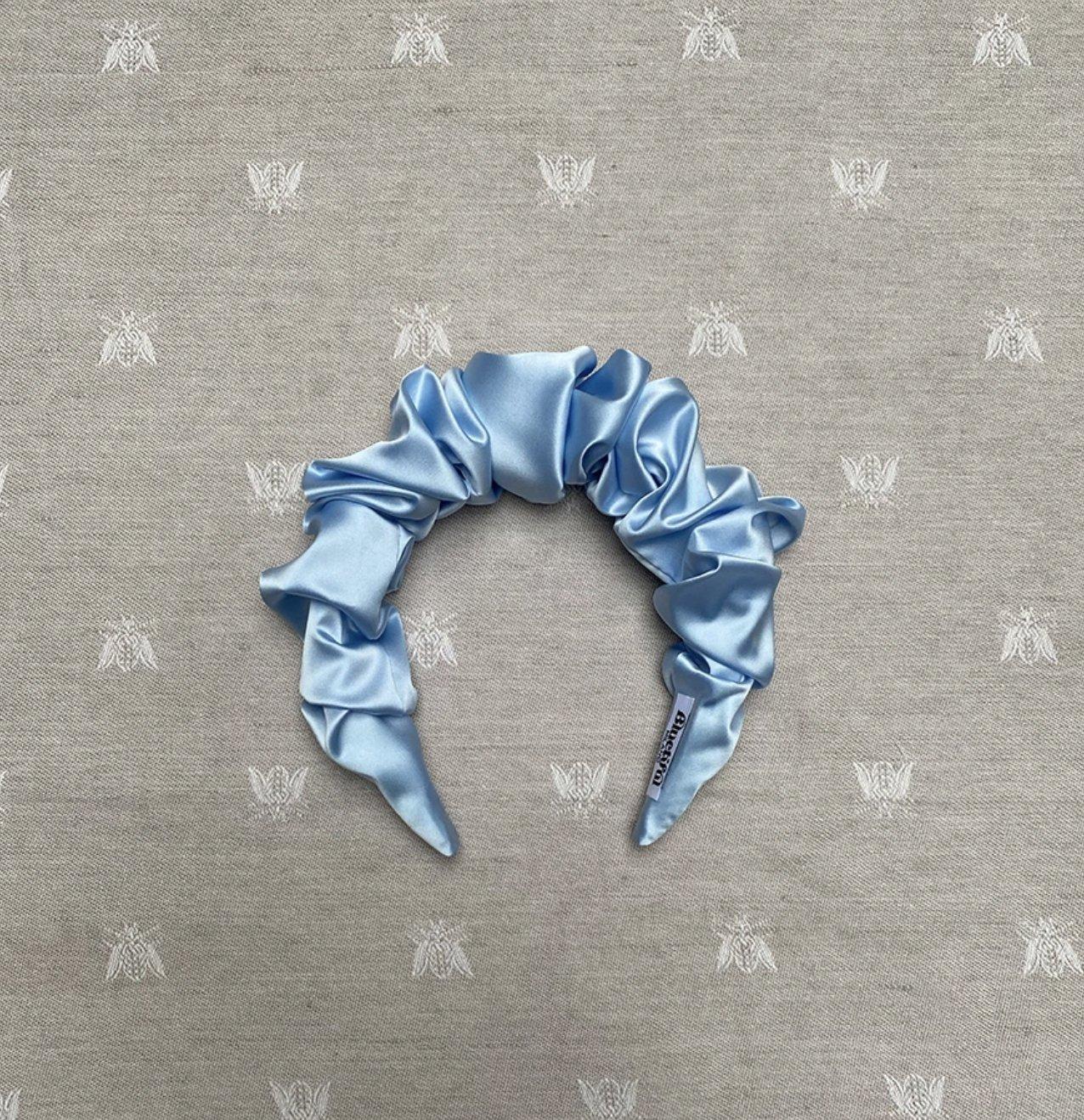 Light blue ruched silk headband shot on a grey piece of fabric printed with white bees