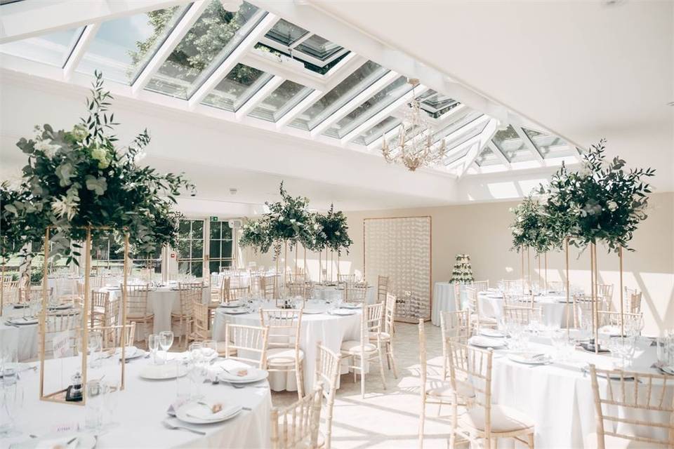 Tables and chairs set up for a white wedding reception in Hayne House Orangery
