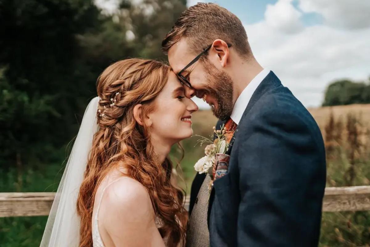a redhead bride with a wavy plaited half up half down wedding hairstyle as she faces her groom smiling - sophie griffiths
