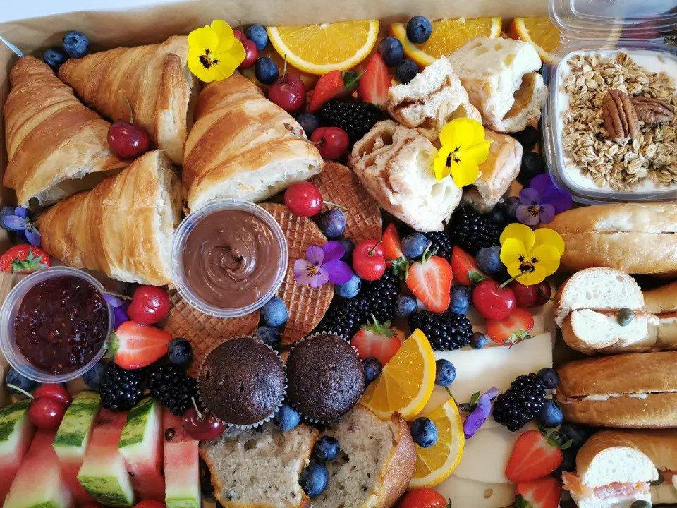 Close-up shot of a brunch grazing box, including croissants, muffins, granola, orange slices, watermelon, blueberries, decorative flowers and bread