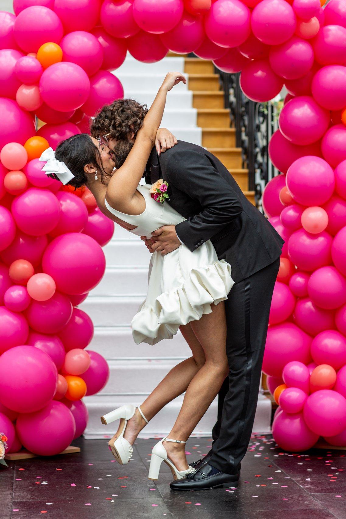 Couple kissing in front of a balloon arch