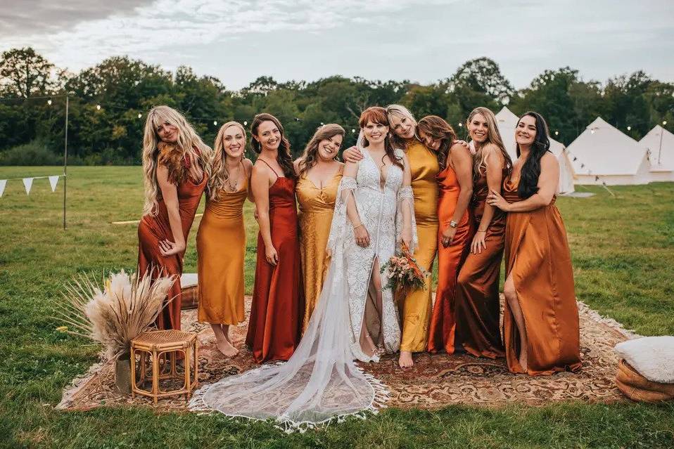 A bride standing on a boho style rug outside flanked by three bridesmaids on either side in rust toned mismatched bridesmaid dresses