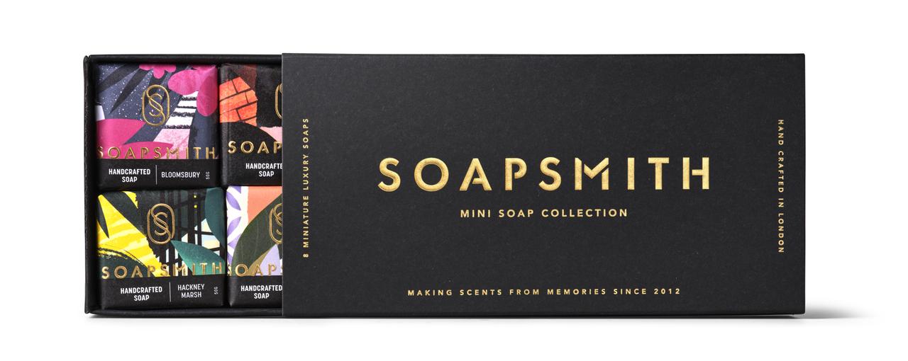 A rectangle-shaped black box with gold metallic writing showcasing 8 individually and colourfully packaged soaps.
