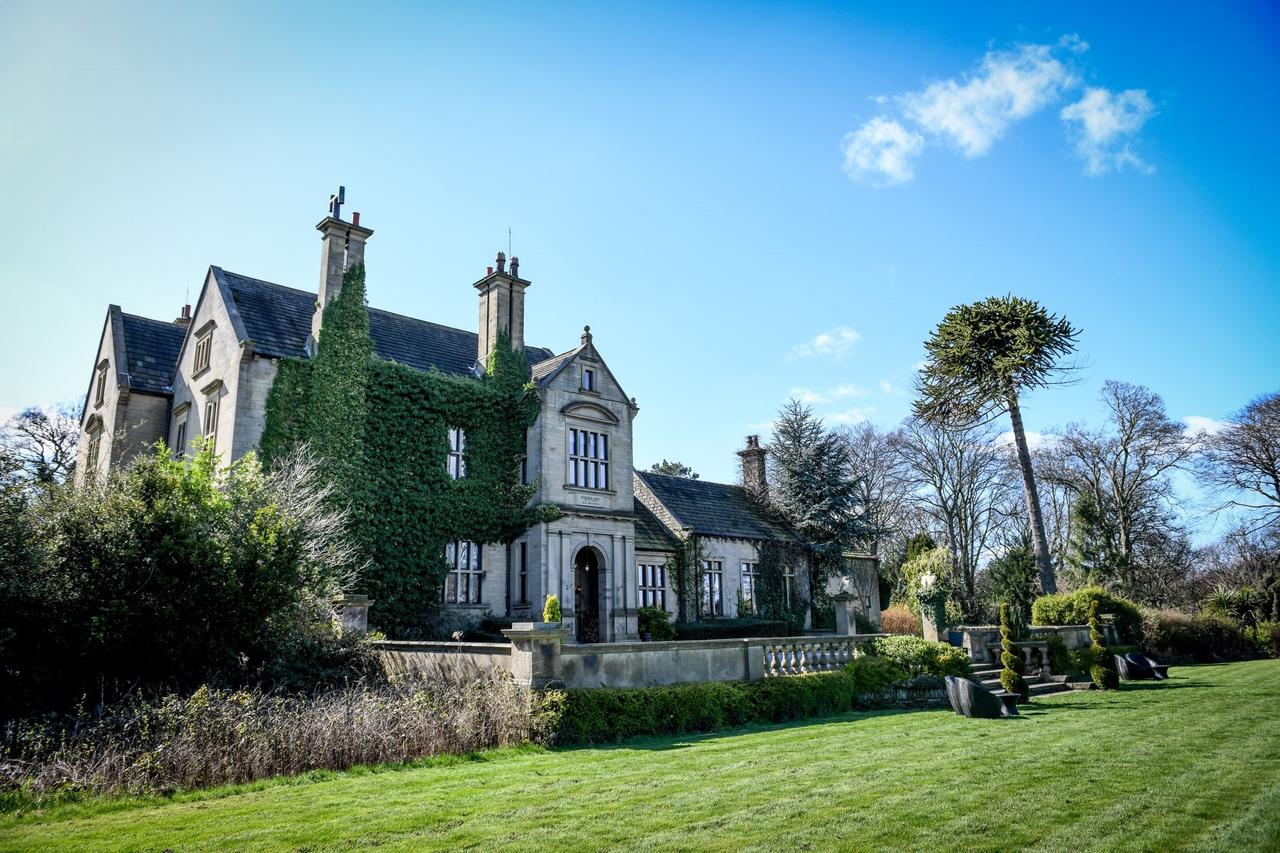 Stately home wedding venue with a manicured lawn and trees outside