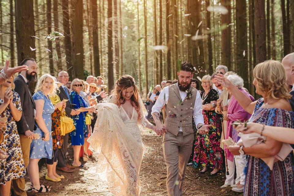 A newly married couple walking through two lines of guests as they scatter confetti on them