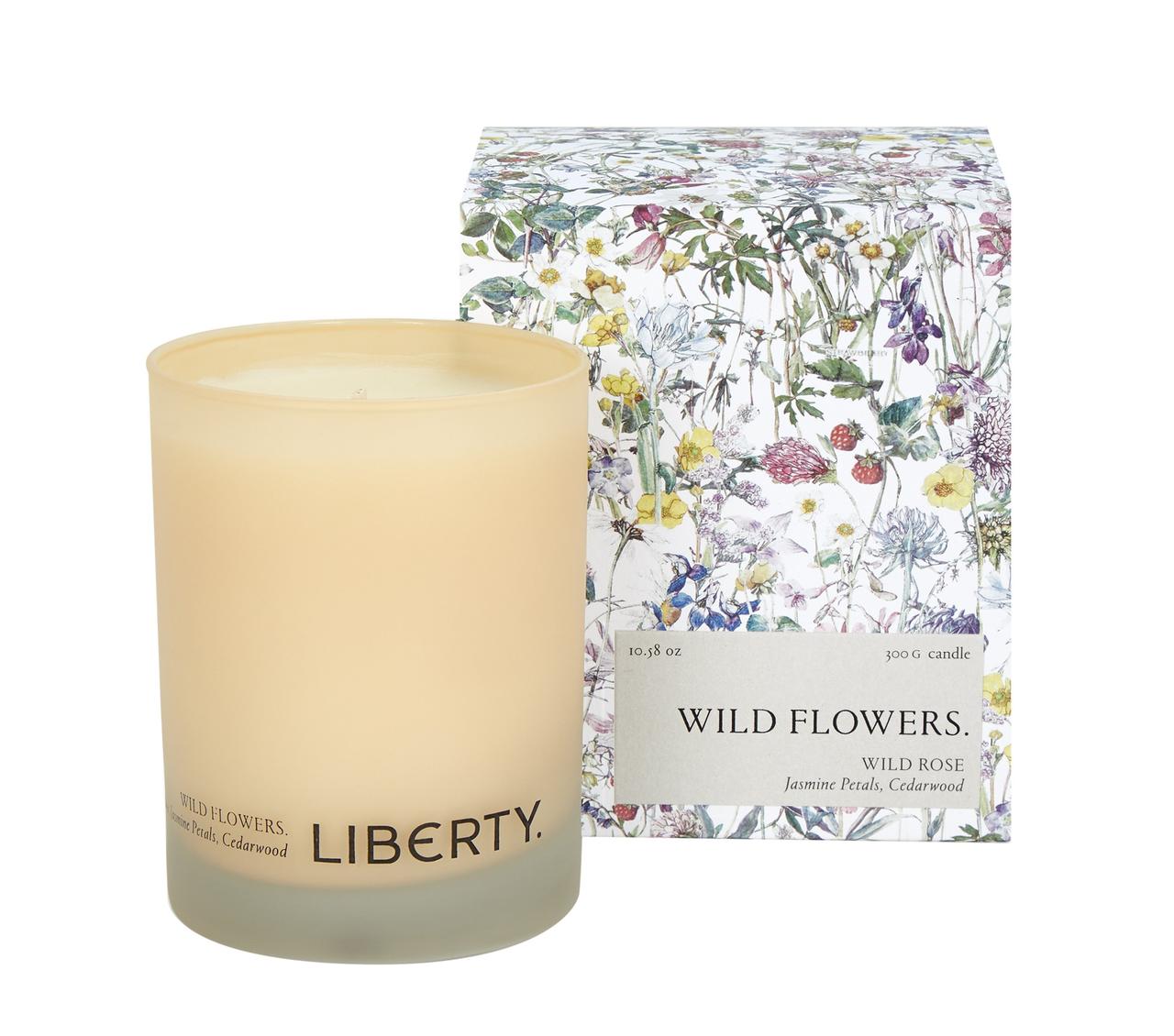 A white candle next to its packaging which features a vibrant floral print.