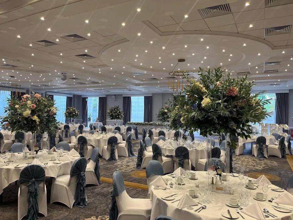 Reception room with round white tables, floral centrepieces, set tables, fairylights and chairs with sashes