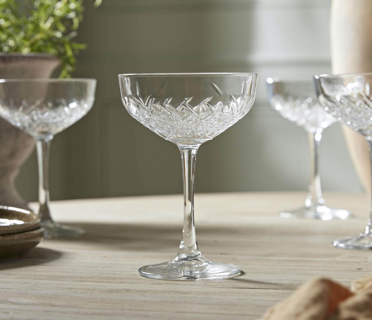 a set of four crystal glass champagne coupes on a table.