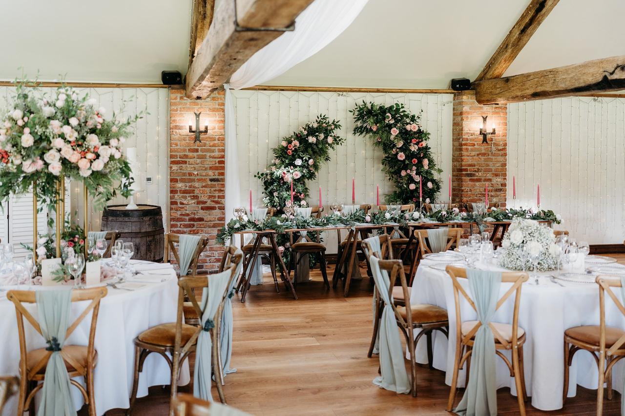 Interior of a stone barn-style wedding venue set up for a wedding reception with lots of flowers and greenery against white linen.