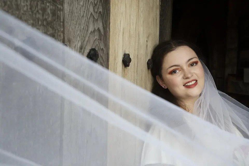 A bride smiles at the camera leaning against a wooden wall