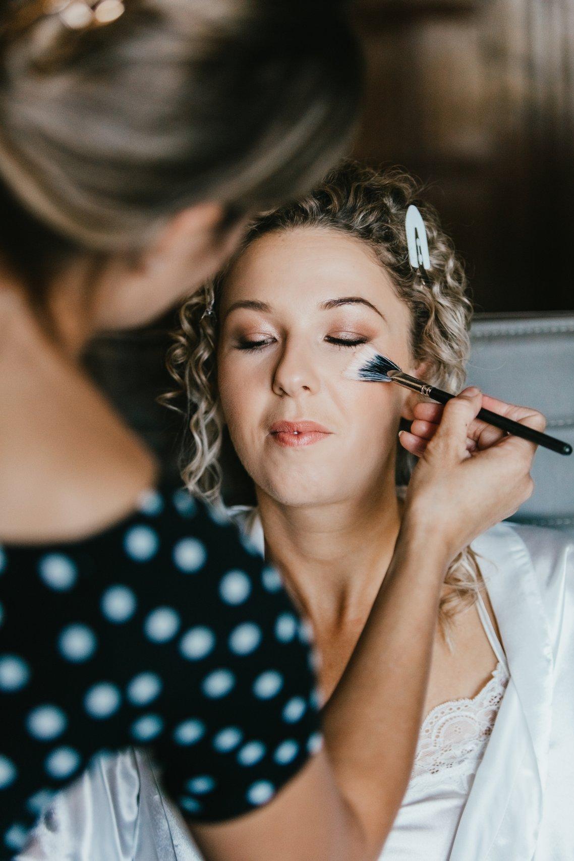 A bride has her makeup applied with a brush