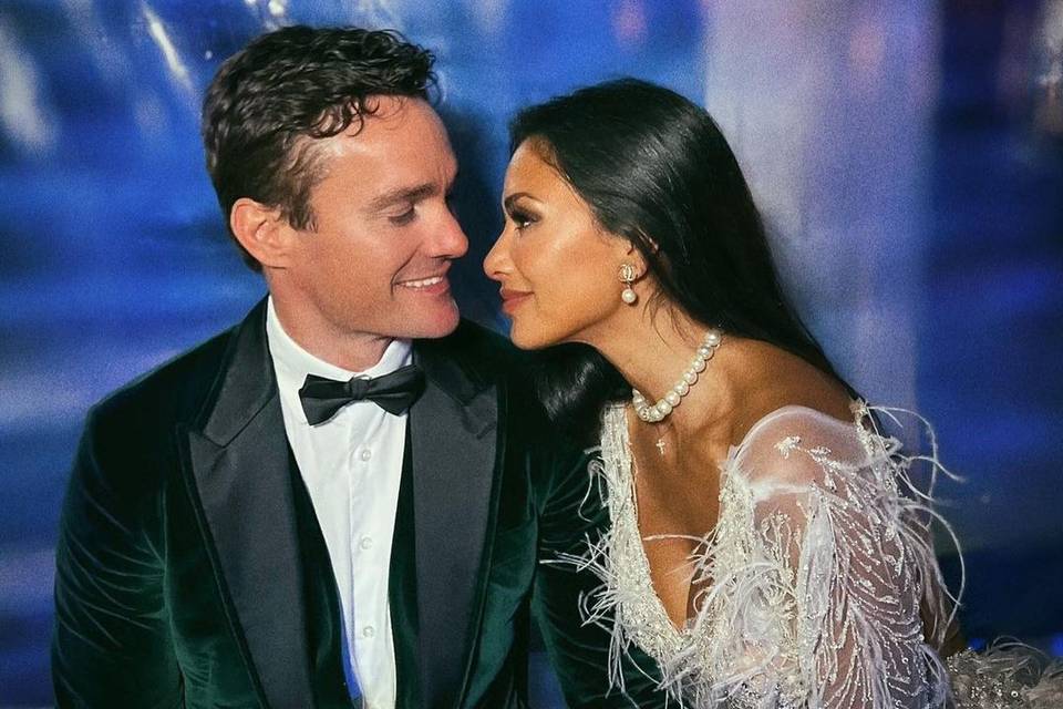 Thom Evans wears a velvet suit and bow tie as he sits next to Nicole Scherzinger who wears a white mini feathered dress