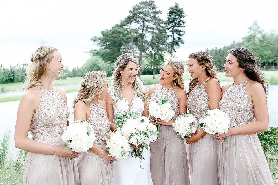 A bride smiling in the middle of five bridesmaids, all holding bouquets and looking at each other