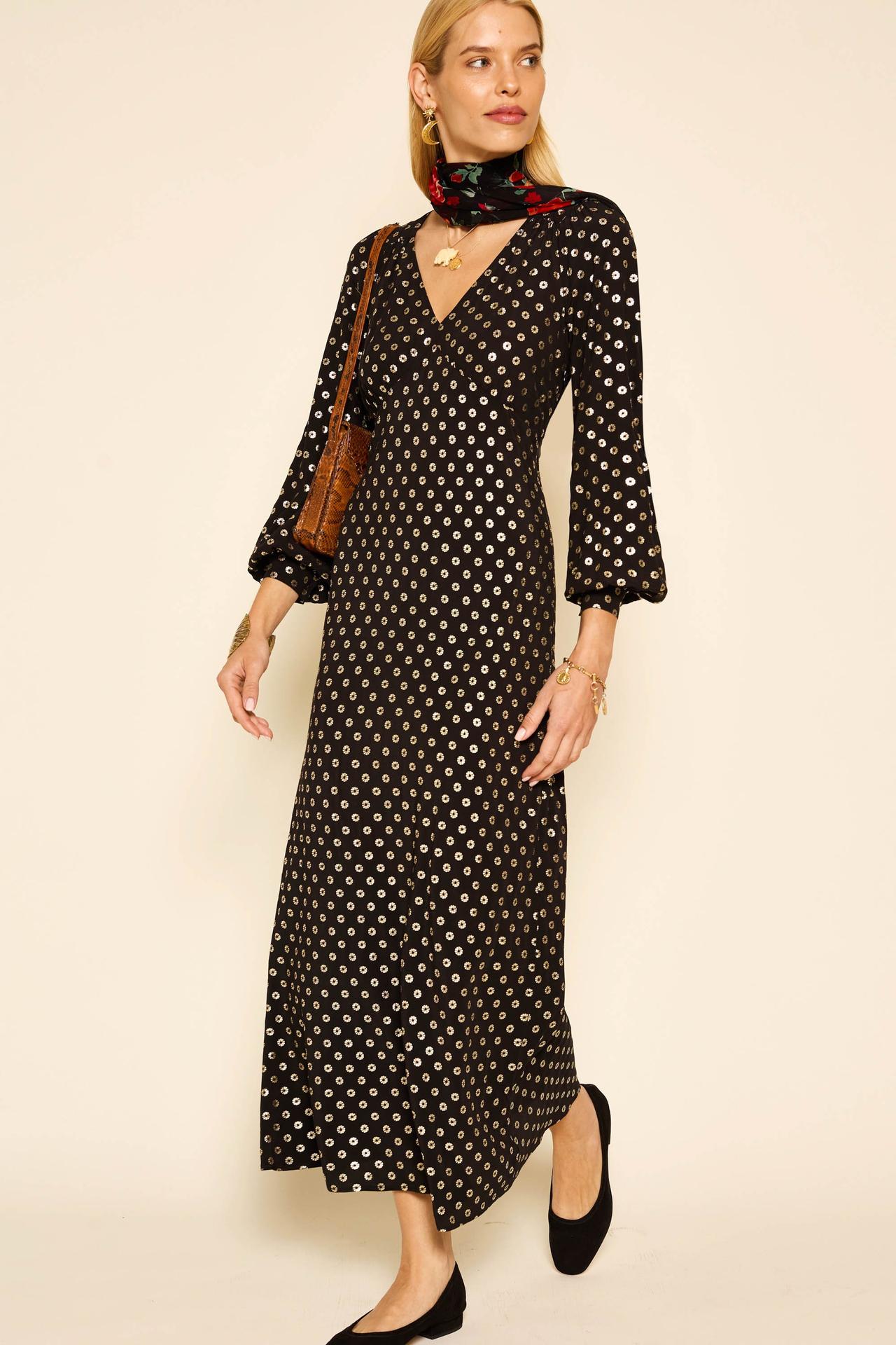 A wedding guest wearing a long sleeved black midaxi dress covered with gold polka dots. She's wearing it with a neck scarf and black ballet pumps.