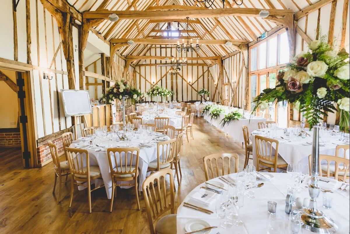 a white rustic barn with dark beams and a wedding breakfast table set up