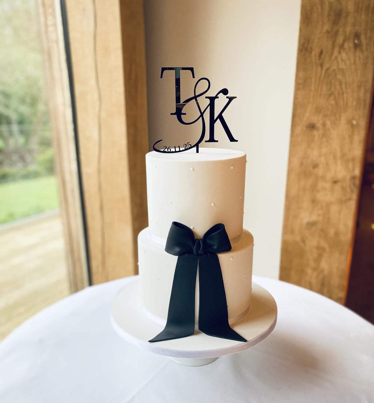 A simple white iced two tier wedding cake studded with pearls and decorated with a navy blue velvet bow and simple cake topper.