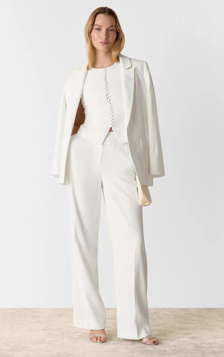 model casually styling a white waistcoat with a matching blazer and trousers