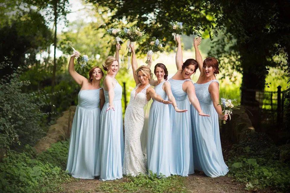 Bride posing with five bridesmaids in pale blue dresses with their arms out either side like an aeroplane in a funny bridesmaid photo idea