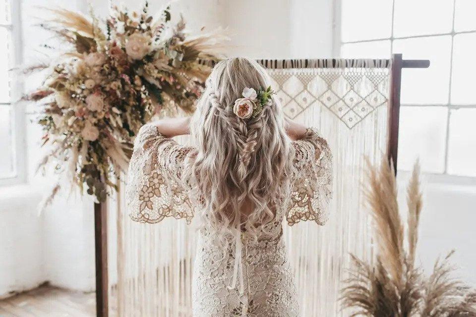 Back of a boho bride with long blonde hair in a fishtail half up with floral accessories
