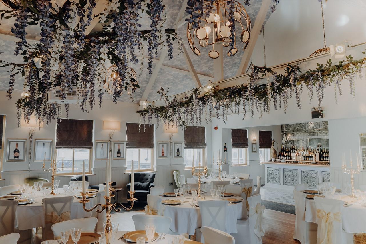 A dusty pale blue room with hanging florals, candelabras, a small bar, and wine artwork