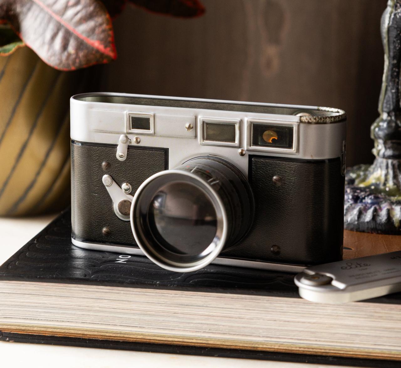A storage tin that looks like a vintage camera placed atop a book shelf.