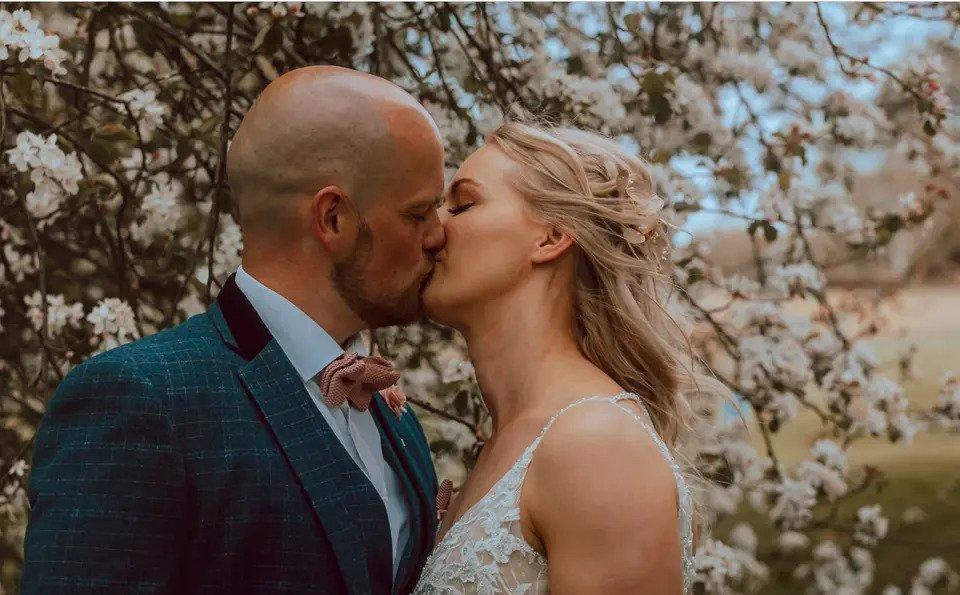 Close up picture of a bride and groom kissing in front of a tree covered in pink blossom