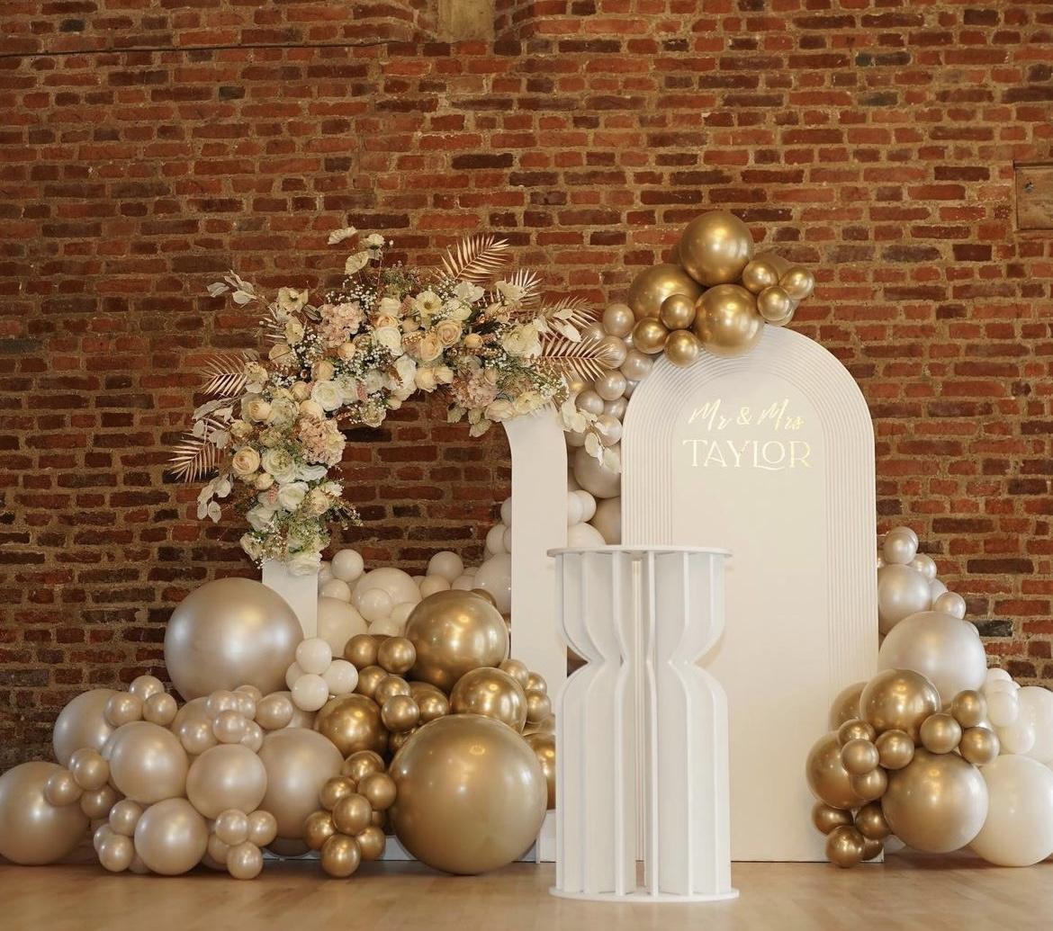 Gold and beige set up against a brick wall with a mix of flowers and balloons.