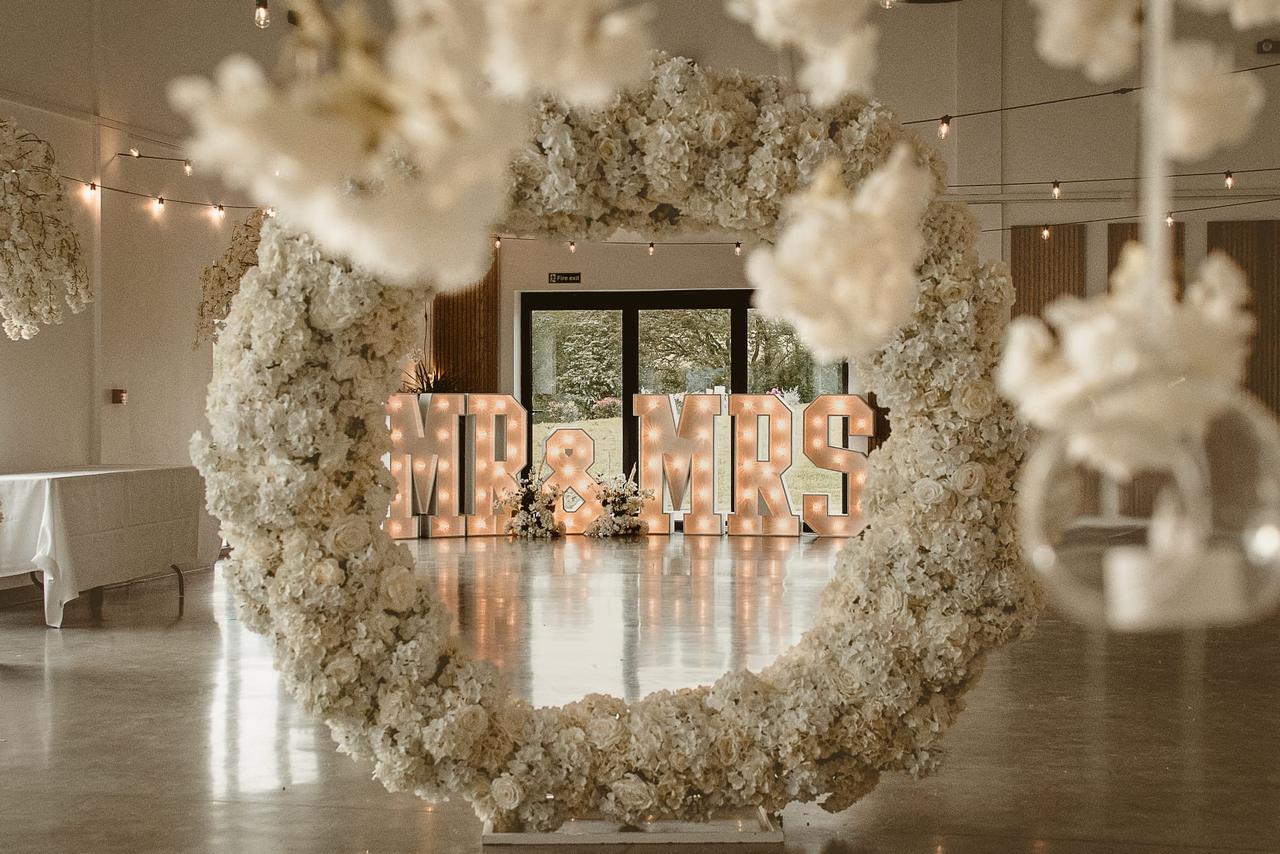 White Floral Wreath Floral Arch with Mr and Mrs list up sign in background