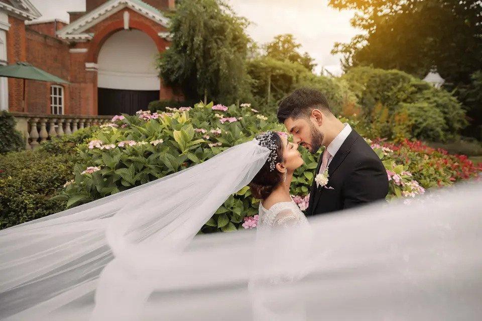 Bride and groom lean in for a kiss in the gardens outside a wedding venue