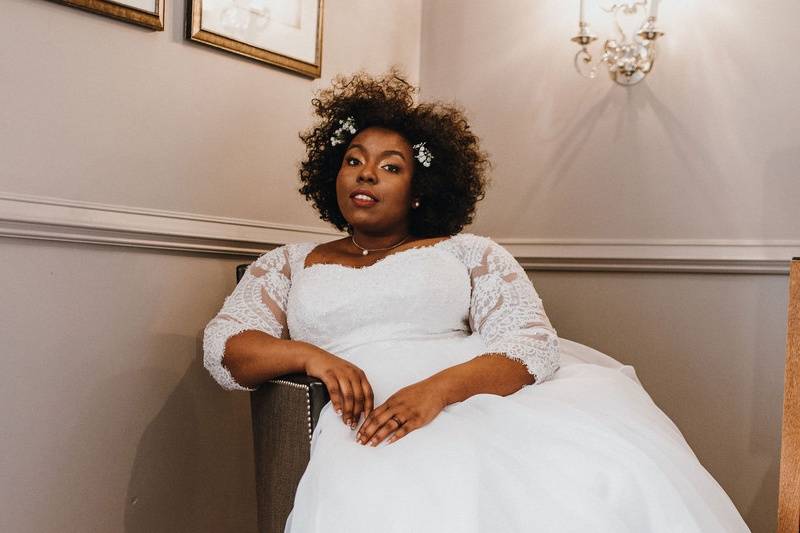 Michelle sitting in a chair. She's wearing a white wedding dress with lace sleeves and she is looking at the camera