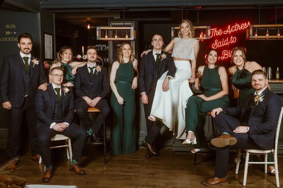 Group shot of the bride, groom and four bridesmaids and four groomsmen all posing together in a darkly decorated bar