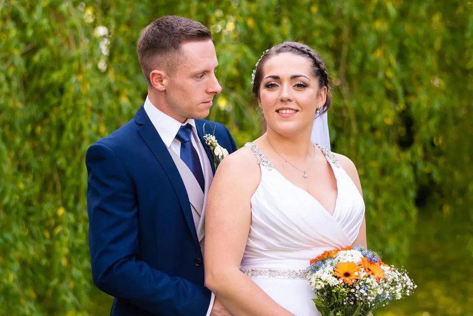 Bride and groom stand outside with the groom's arms around the bride holding a bouquet