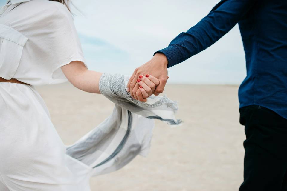 Man and woman holding hands as they run across the sand on a beach