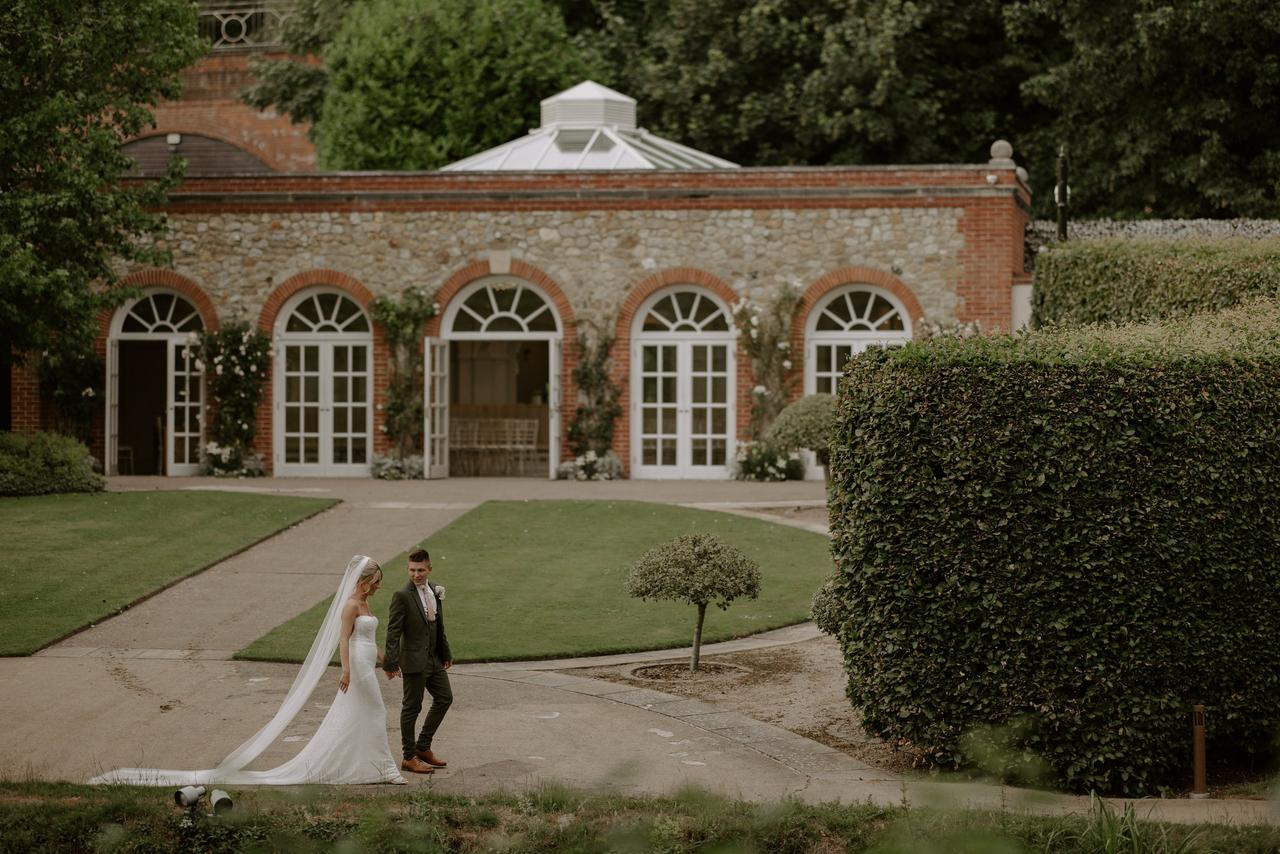 A bride and groom walking in the grounds of an orangery wedding venue
