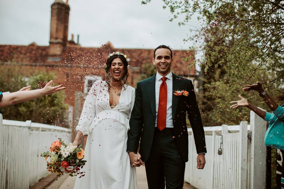 a couple holding hands and laughing as people throw confetti over them as they walk across a bridge