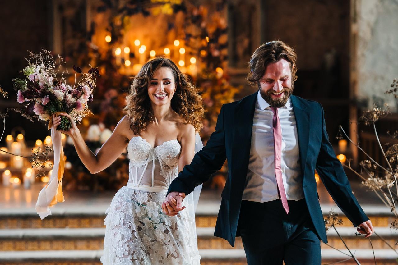 A bride and groom rush down the aisle of their twilight wedding ceremony smiling.