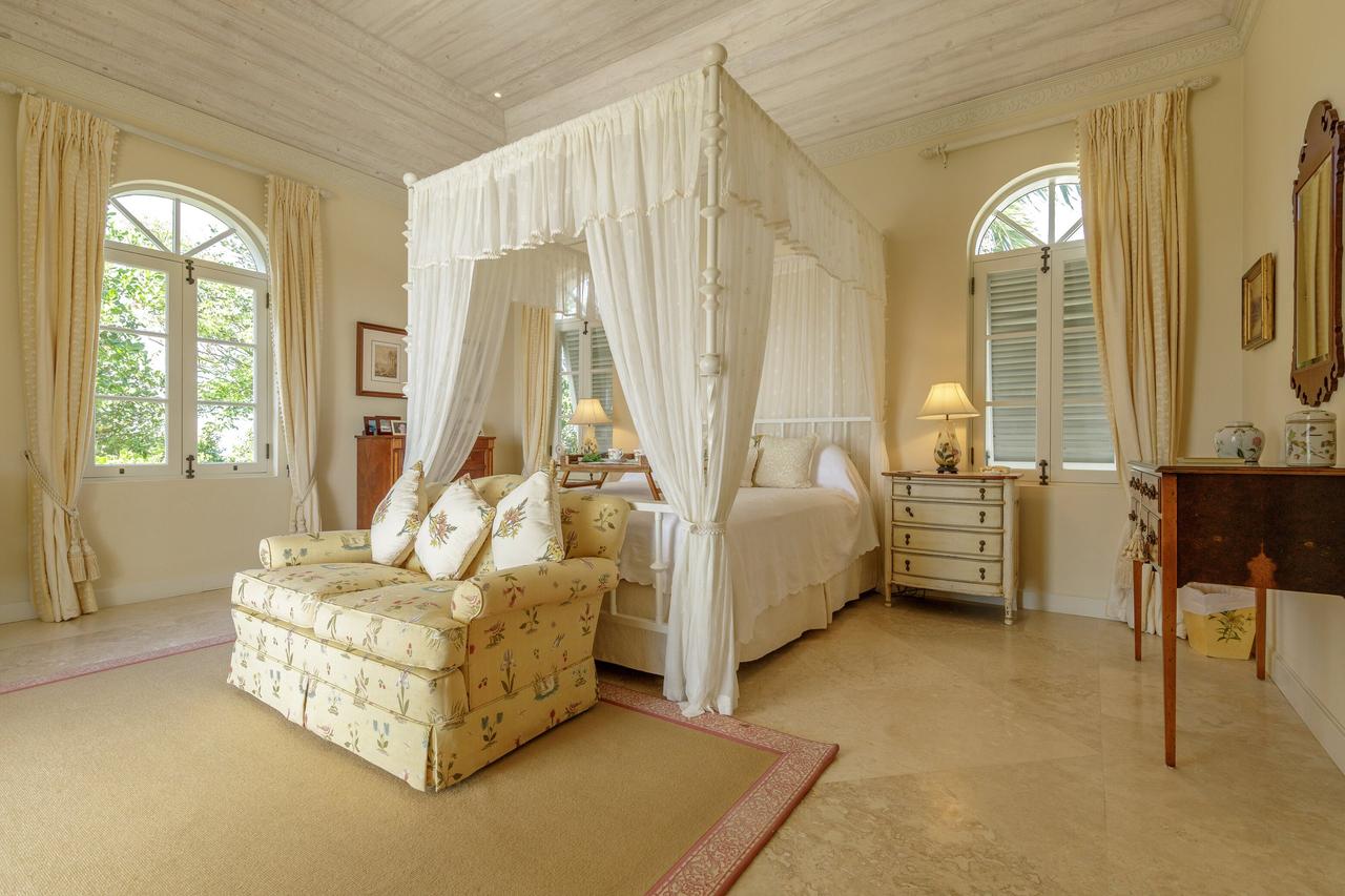 Luxurious hotel room in Lavender Hill, Mustique hotel - a plush white four-poster bed with cushions, cream curtains and a white carpet