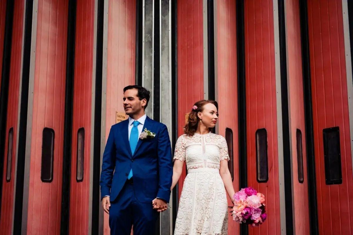 an artistic shot of a bride and groom holding hands and standing in front of red pull shutters