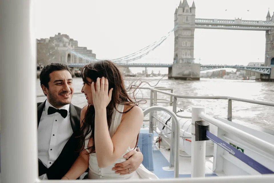 bride and groom embrace on a boat with tower bridge in the background