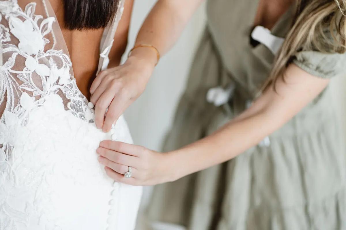 a shop assistant doing up the back buttons of a bride's wedding dress