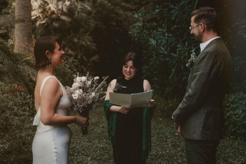 a couple standing in a woodland surrounding with a celebrant reading from a binder