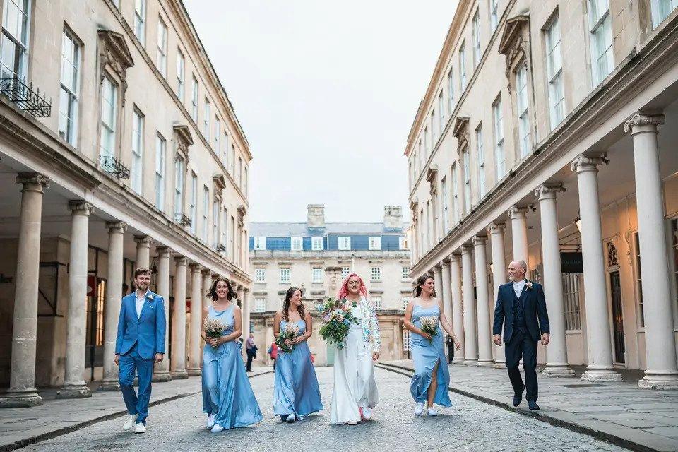 A bride with her bridesmaids and bridesmen all dressed in blue suits and dresses with white trainers walking down a city street together